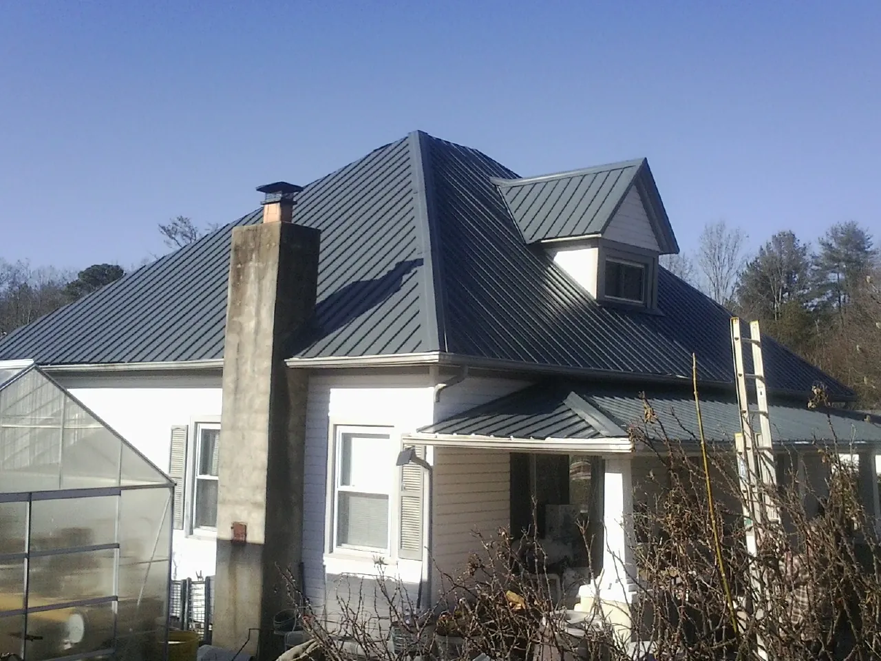 Dark blue standing seam metal roof on a white farmhouse with dormer — Slate & Tile Roof Repair by Roofing Brothers in Olathe
