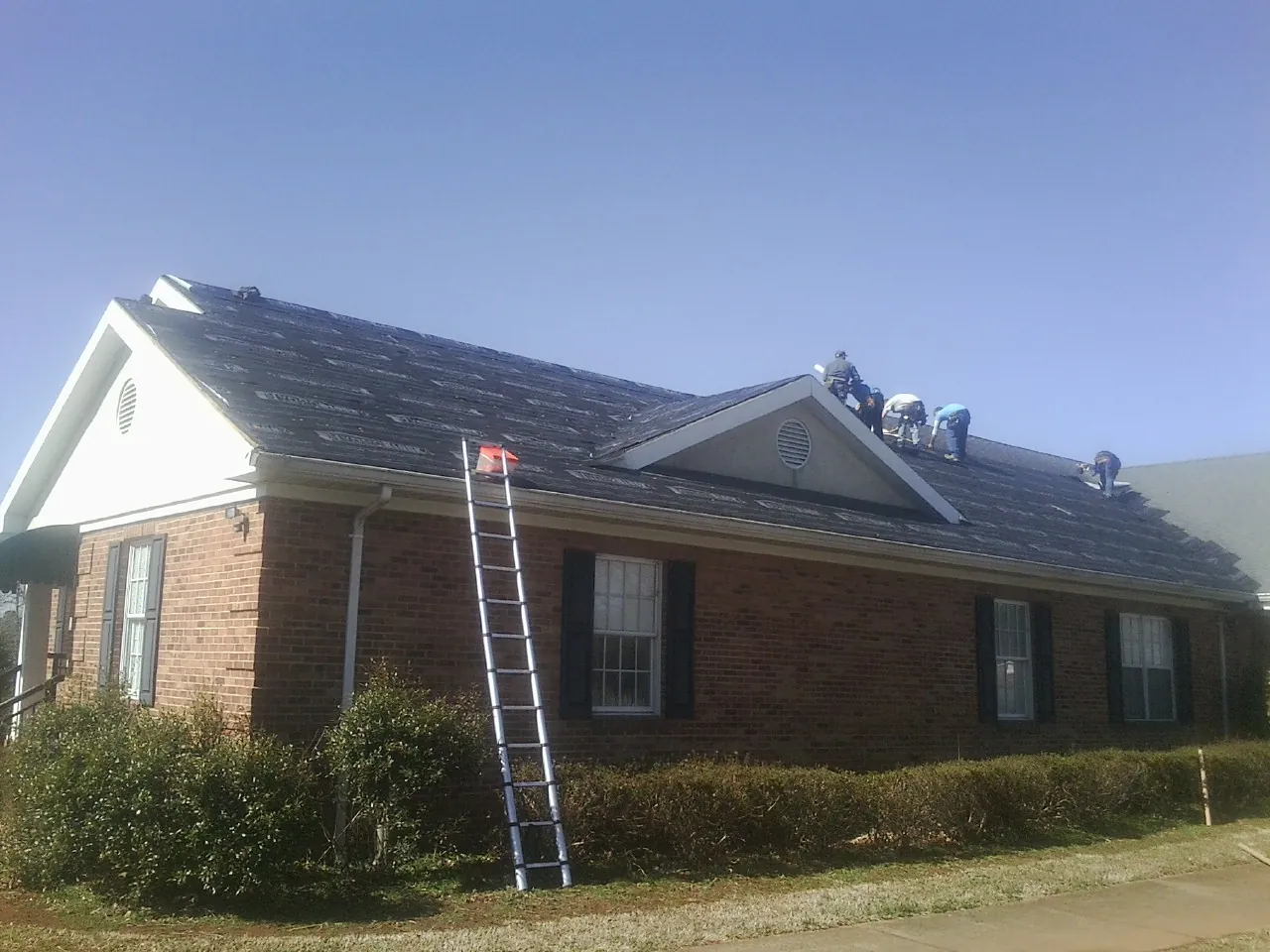 Crew tearing shingles off a brick ranch roof with a ladder set — Emergency Roof Repair work by our crew in Olathe