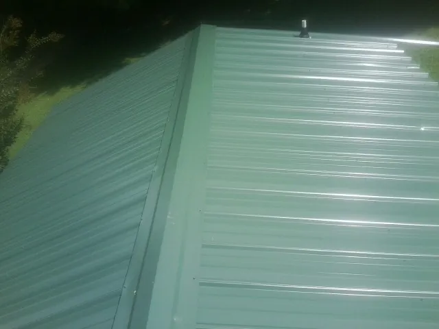 New green metal panels meeting at the ridge of a roof — Flat Roof Repair work by our crew in Olathe