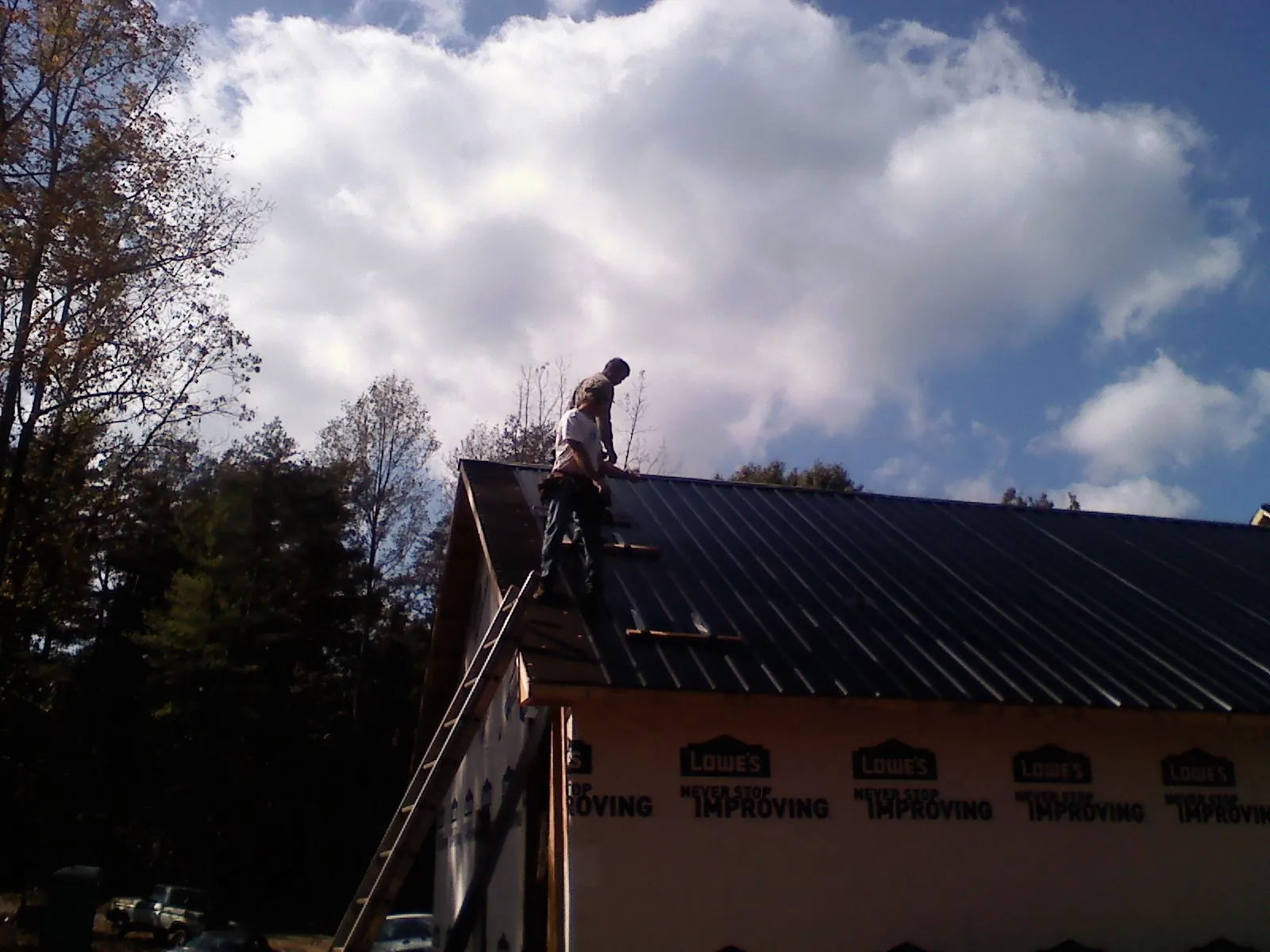 Roofer fastening dark metal panels high against a cloudy sky, from a Roof Inspection job in Olathe