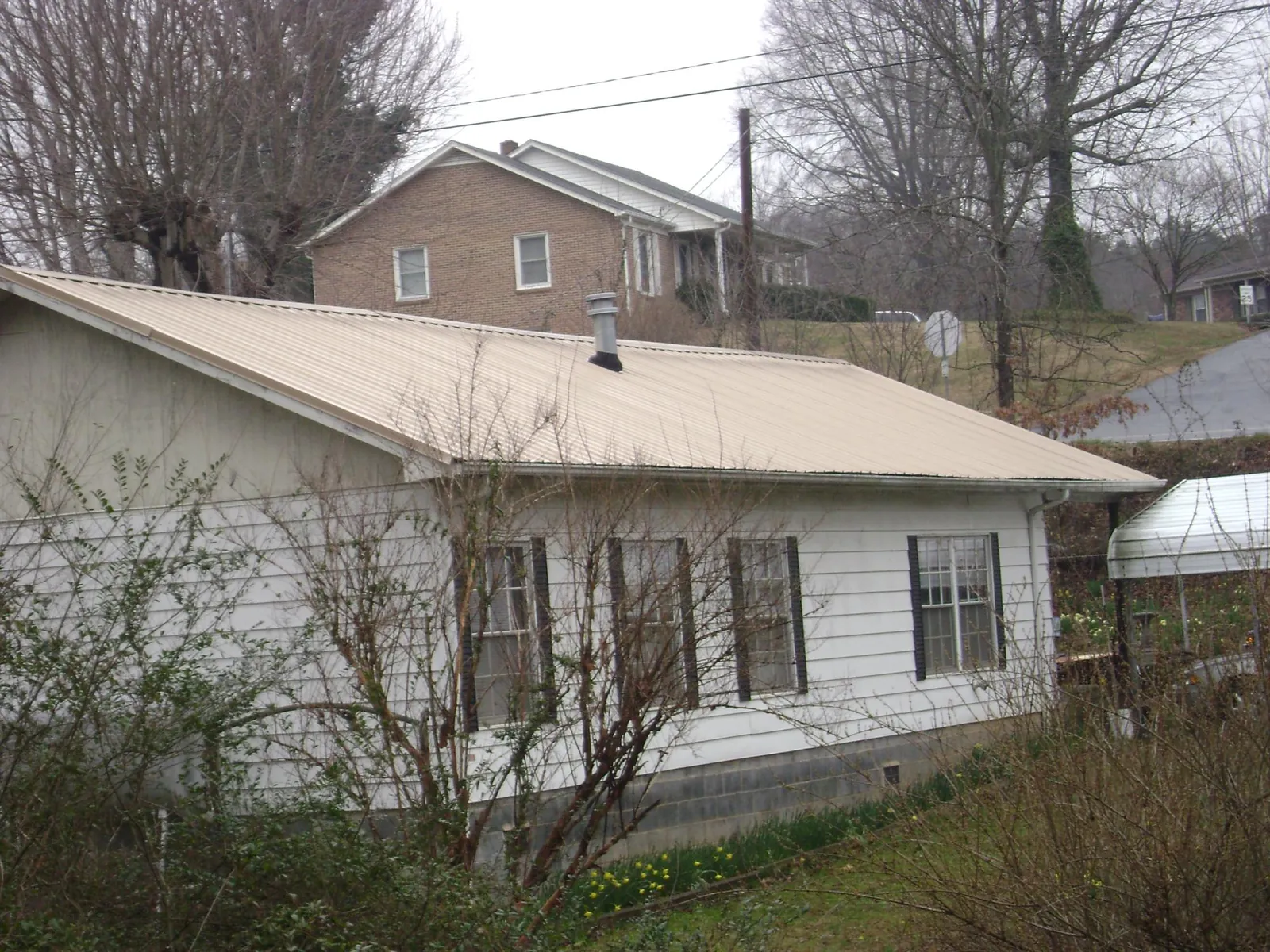 Tan metal roof on a white sided house set into a hillside — Commercial Roofing by Roofing Brothers in Olathe